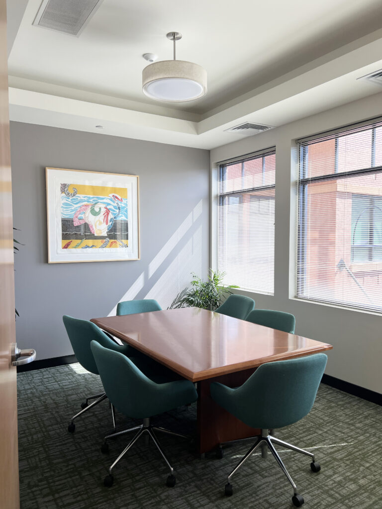 Modern office conference room with wooden meeting table, teal chairs, artwork, and natural lighting