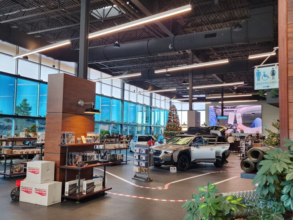 Modern automotive showroom interior featuring vehicle display area, product shelves, glass walls, and contemporary commercial design