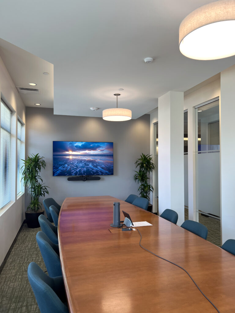 Modern boardroom meeting room with large wooden conference table, blue chairs, display screen, and contemporary office interior