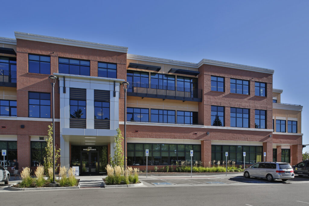 Modern commercial building exterior with brick facade, glass windows, parking area, and contemporary architectural design