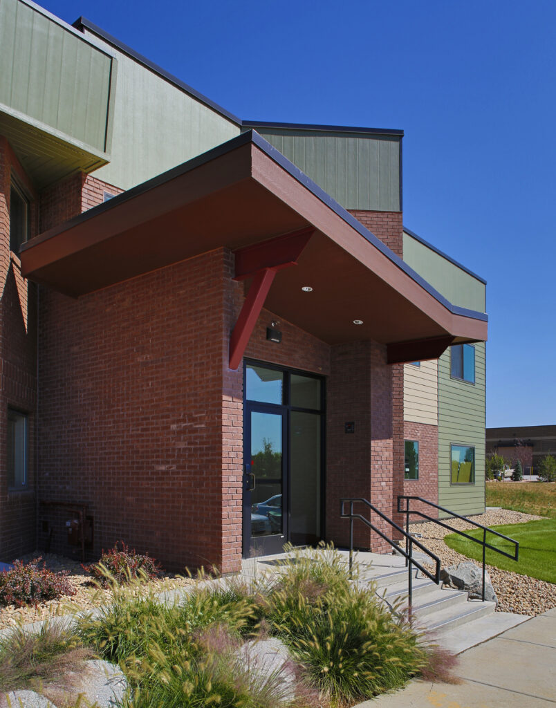 Modern commercial building exterior with brick facade, covered entrance canopy, landscaped walkway, and contemporary architectural design