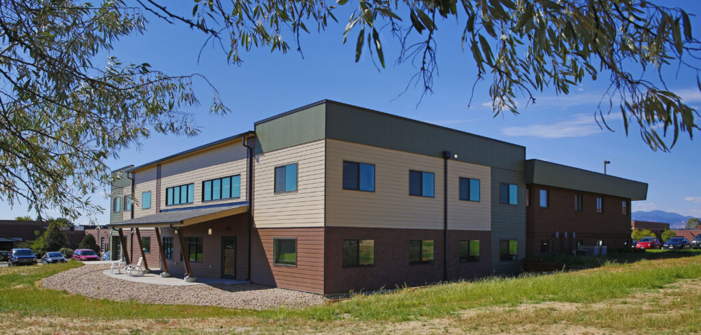 Modern commercial building exterior with mixed brick and metal facade, large windows, landscaped surroundings, and contemporary architectural design