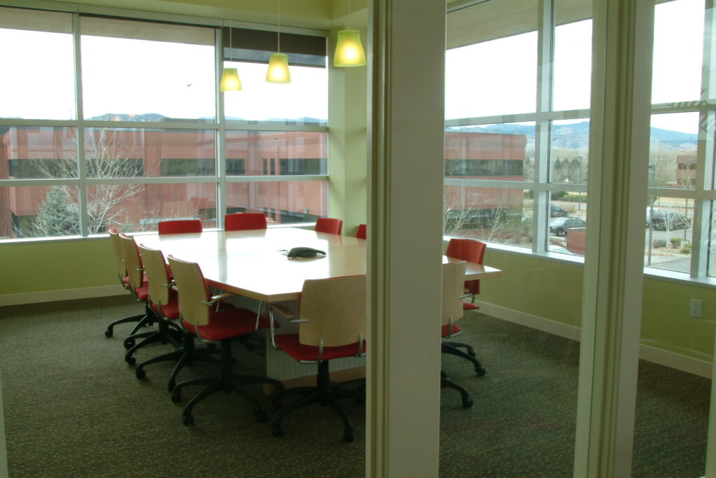 Modern office conference room with large windows, meeting table, red chairs, and contemporary workplace interior design