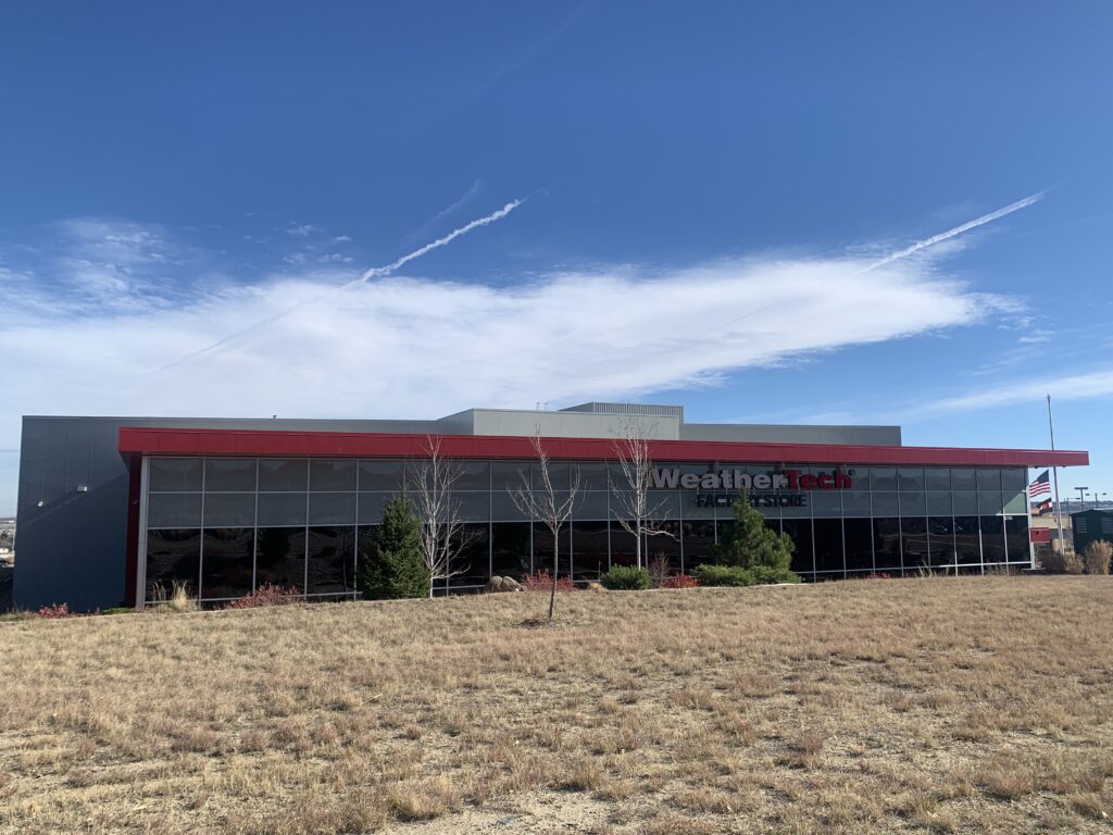 Modern industrial building exterior with glass facade, red accent structure, open landscape, and contemporary commercial architecture