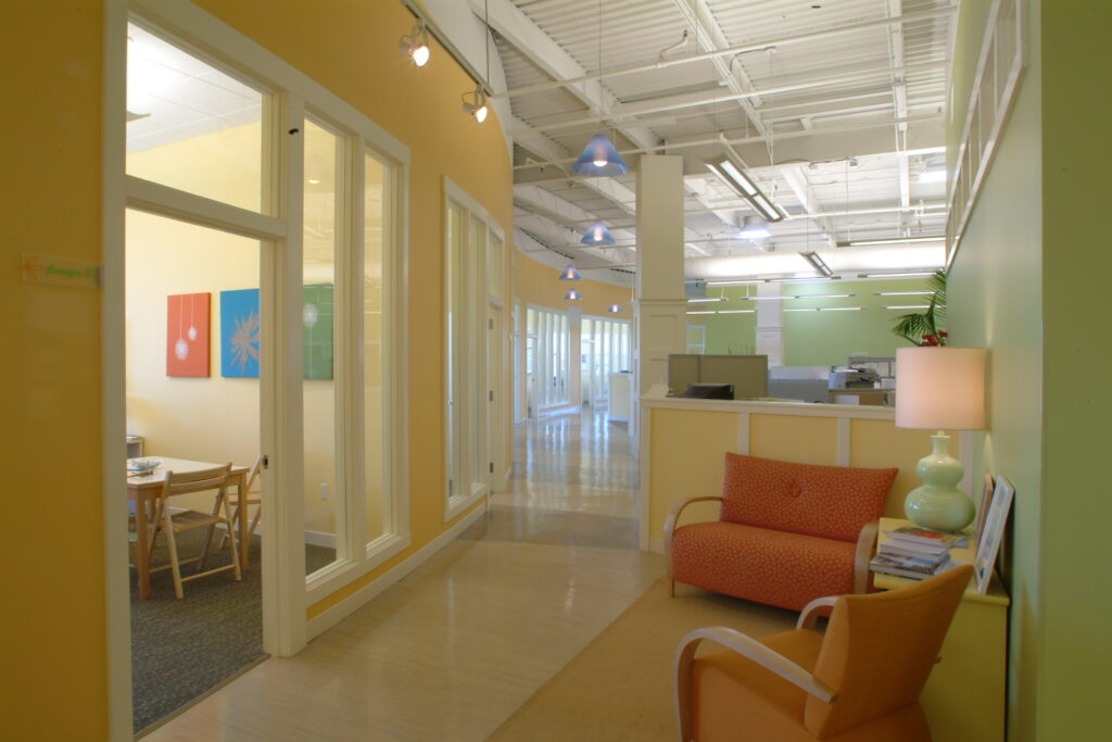 Modern office corridor with glass partitions, colorful walls, seating area, and contemporary interior design elements