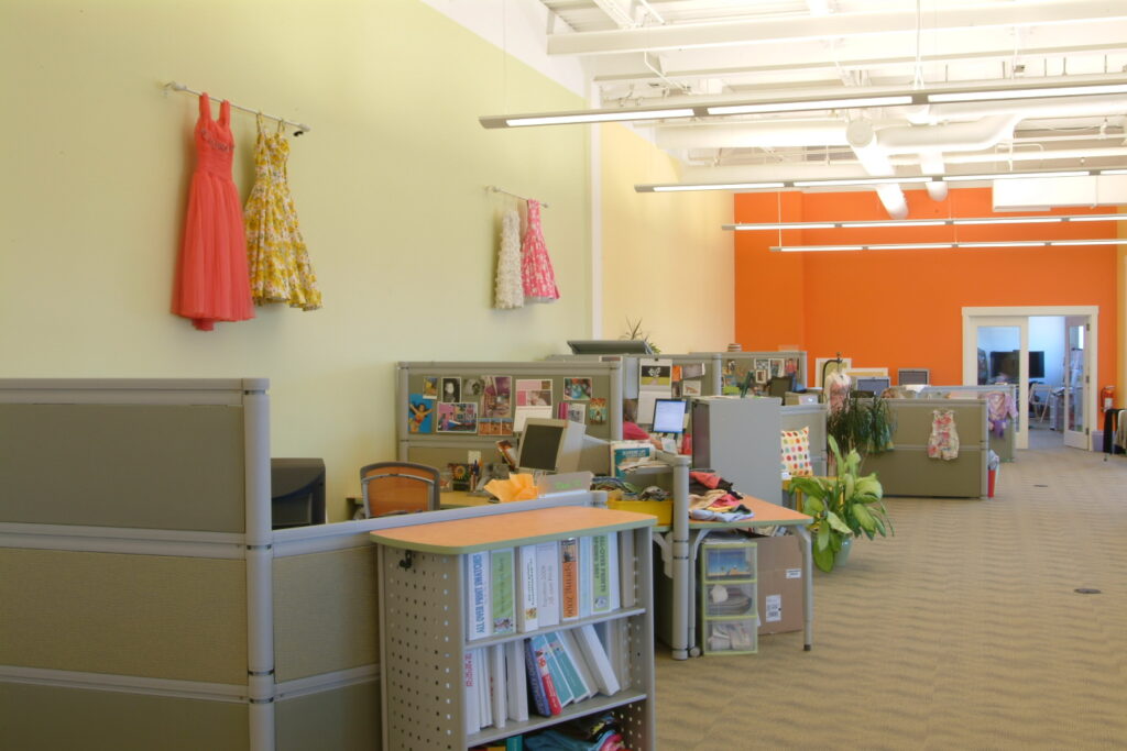 Modern office interior with open workstations, colorful walls, clothing displays, and collaborative workspace design