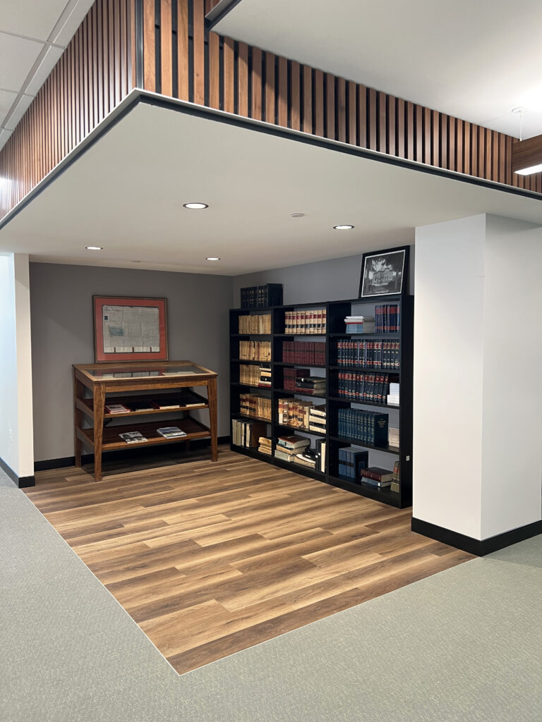 Modern office library area with built-in bookshelves, wooden flooring, display table, and contemporary interior design