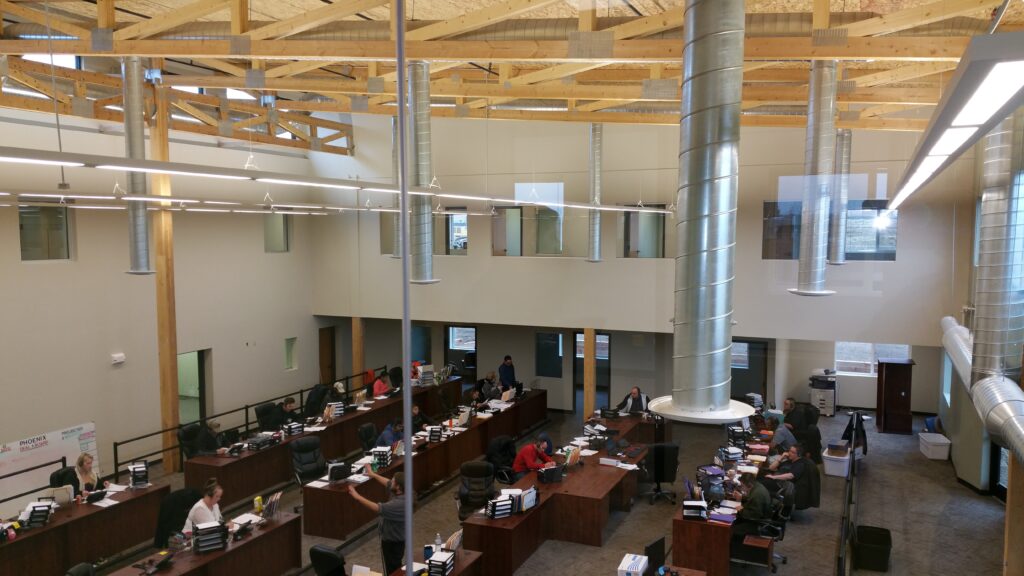 Modern office workspace interior with open desks, high ceilings, exposed wooden beams, and contemporary architectural design
