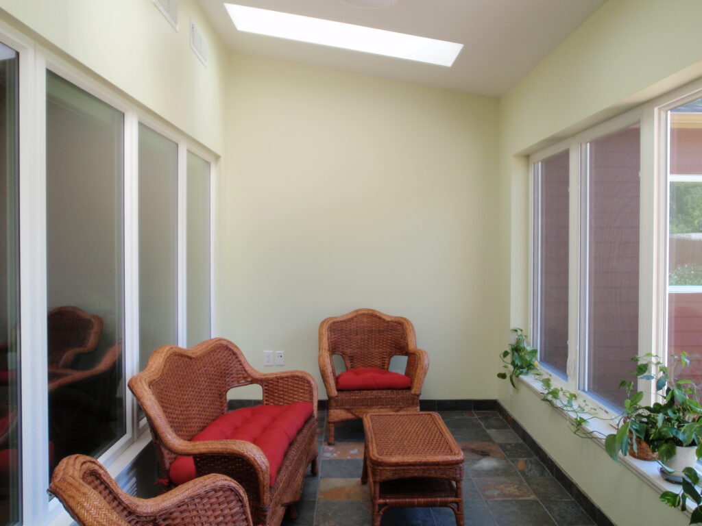 Modern sunroom interior design with skylight, large windows, wicker chairs, and indoor plants