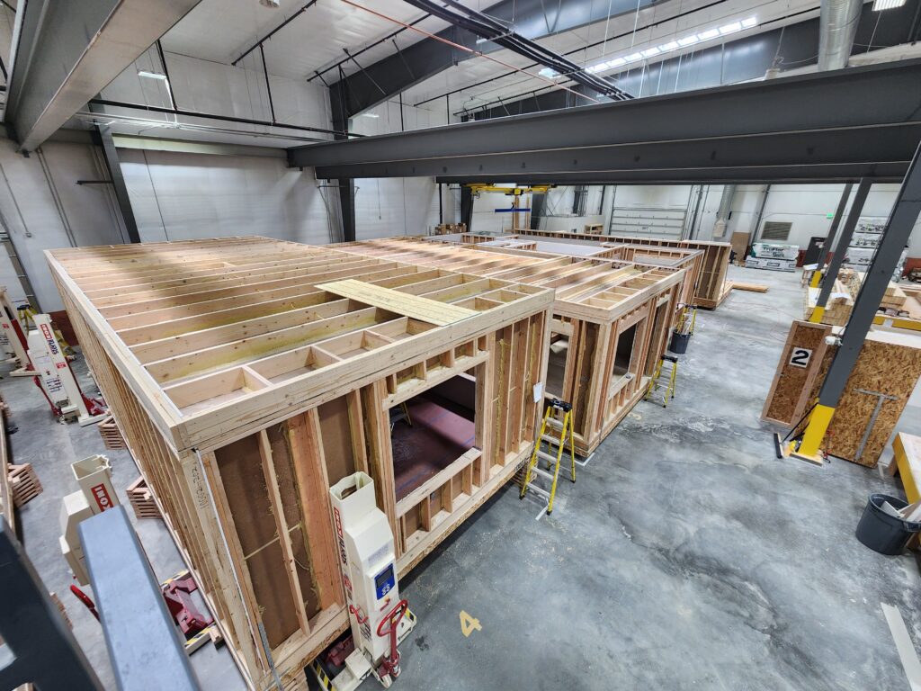 Industrial modular building assembly workshop with timber wall frames, prefabricated structures, ladders, and manufacturing workspace
