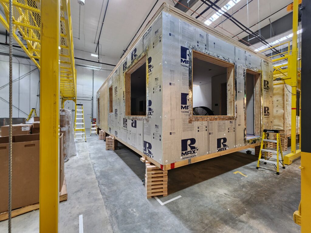 Industrial modular construction workspace with prefabricated building unit, insulation panels, ladders, and manufacturing equipment