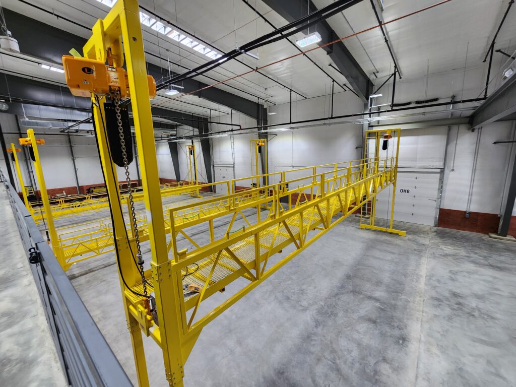 Industrial modular construction facility interior with yellow overhead lifting equipment, safety platforms, and manufacturing workspace