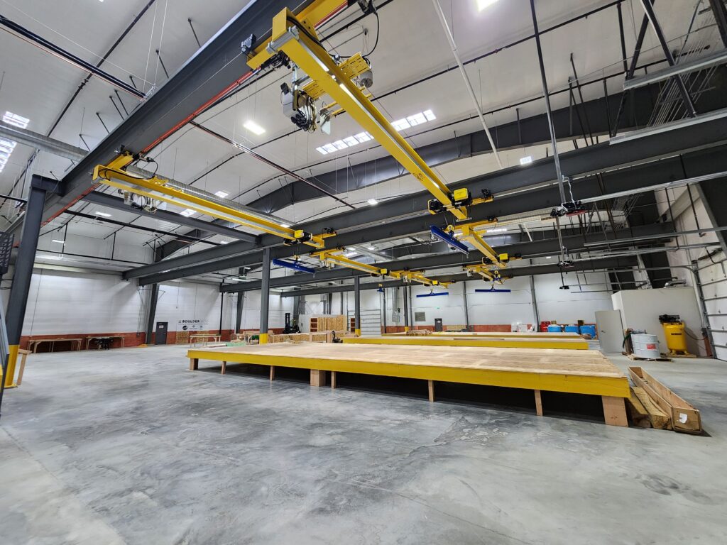 Modern modular construction factory interior with yellow overhead crane system above a prefabricated building production workspace