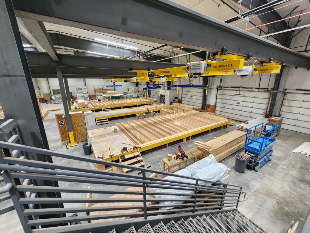 Large modular construction production facility with timber framing stations, overhead cranes, work platforms, and manufacturing equipment