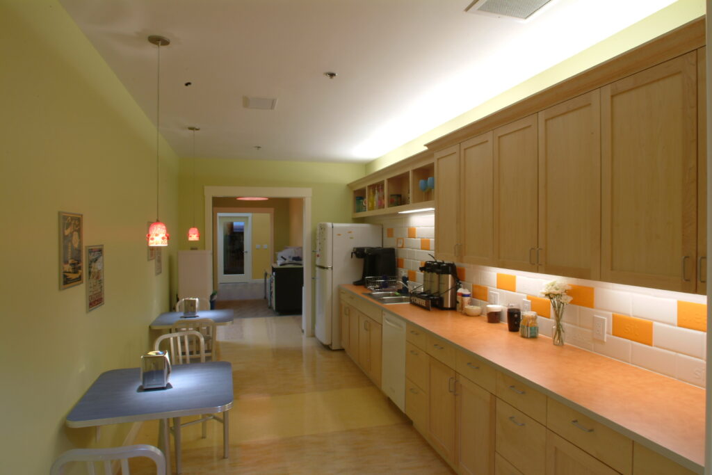 Modern office break room with kitchen cabinets, dining tables, coffee area, and contemporary interior design