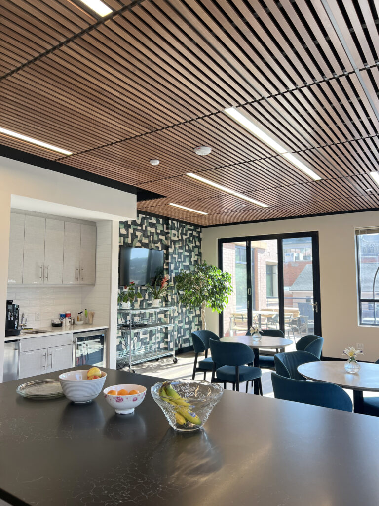 Modern office breakroom with kitchen counter, dining tables, blue chairs, decorative wall, and contemporary interior design
