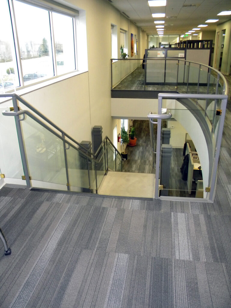 Modern office interior with glass staircase railings, open workspace layout, and contemporary architectural design by PEH Architects