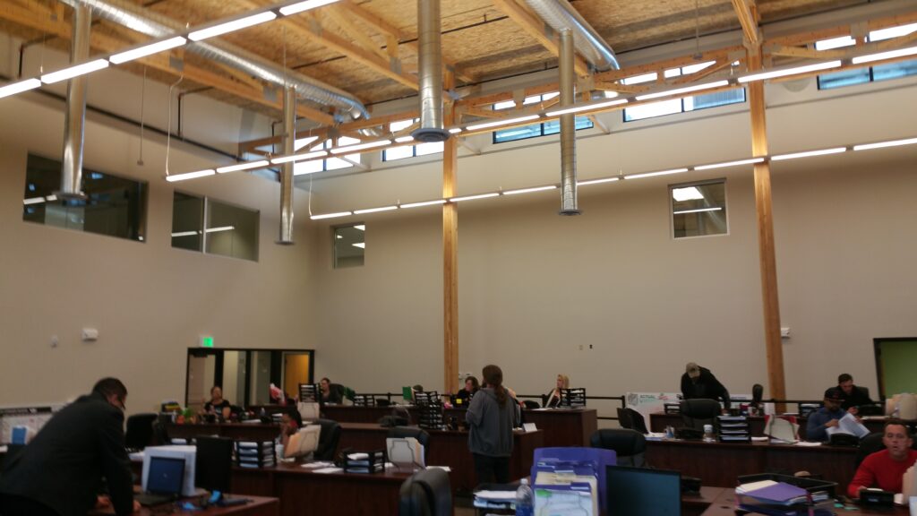 Open plan office interior with exposed wooden ceiling beams, modern lighting, ventilation ducts, and collaborative workstations