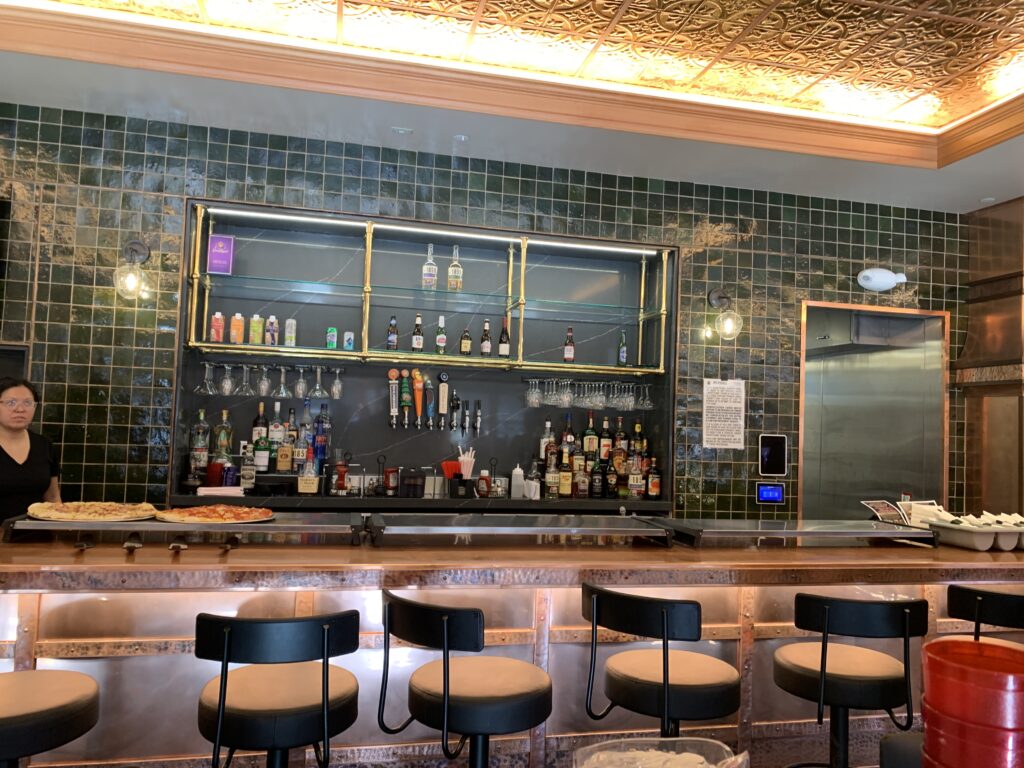 Modern restaurant bar interior with beverage shelves, seating counter, tiled walls, and custom lighting design