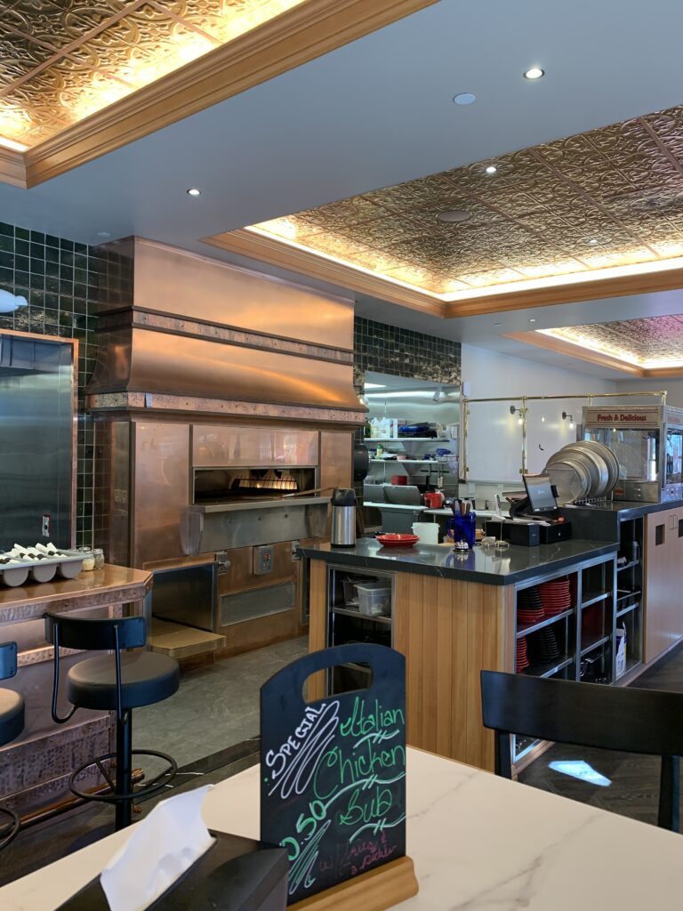 Modern restaurant interior with open kitchen, wood counters, pizza oven, decorative ceiling, and dining area design