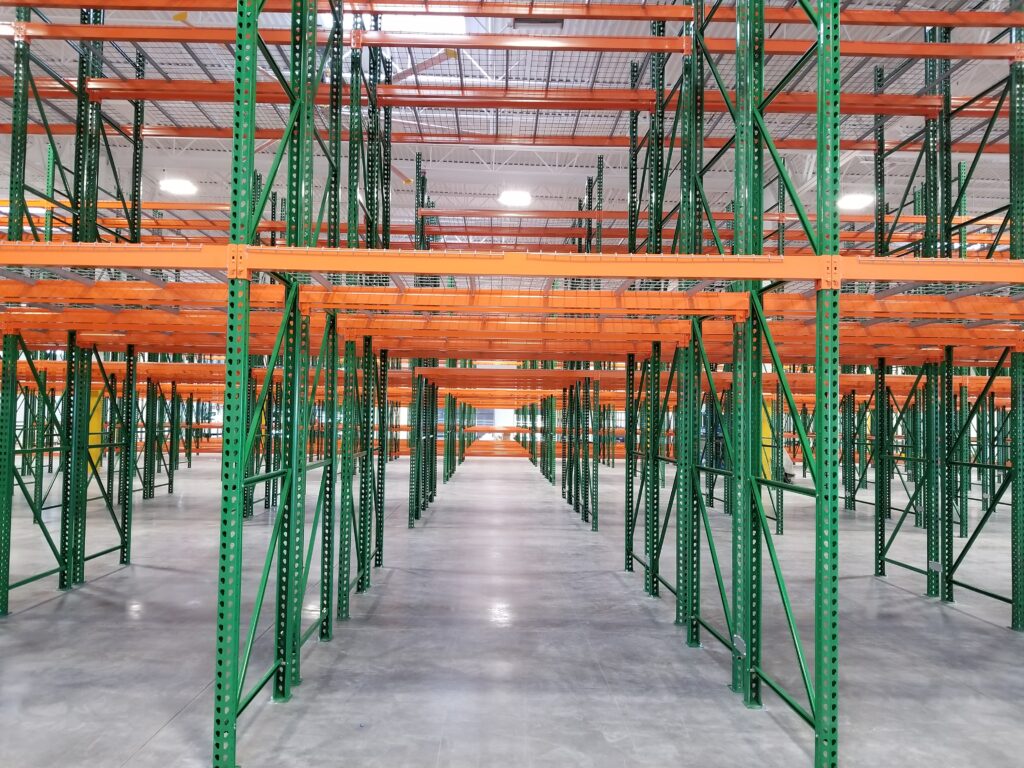 Modern warehouse interior with organized green and orange storage rack system, high ceiling, and polished concrete flooring