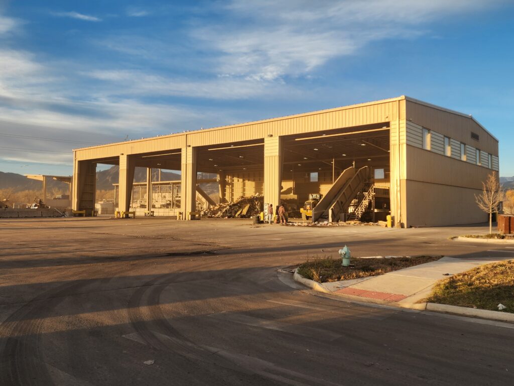 Exterior view of a waste management facility with large industrial bays, processing equipment, and operational yard