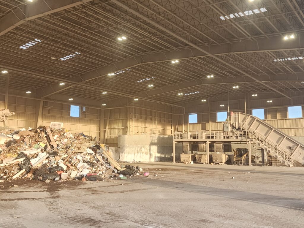Interior view of a waste processing facility with sorting equipment, conveyor systems, and large industrial workspace