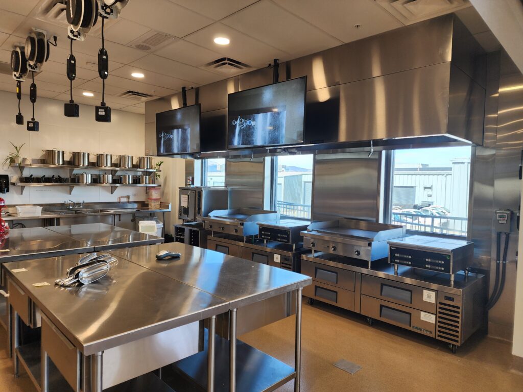Modern culinary training kitchen with commercial cooking stations, stainless steel counters, and kitchen equipment