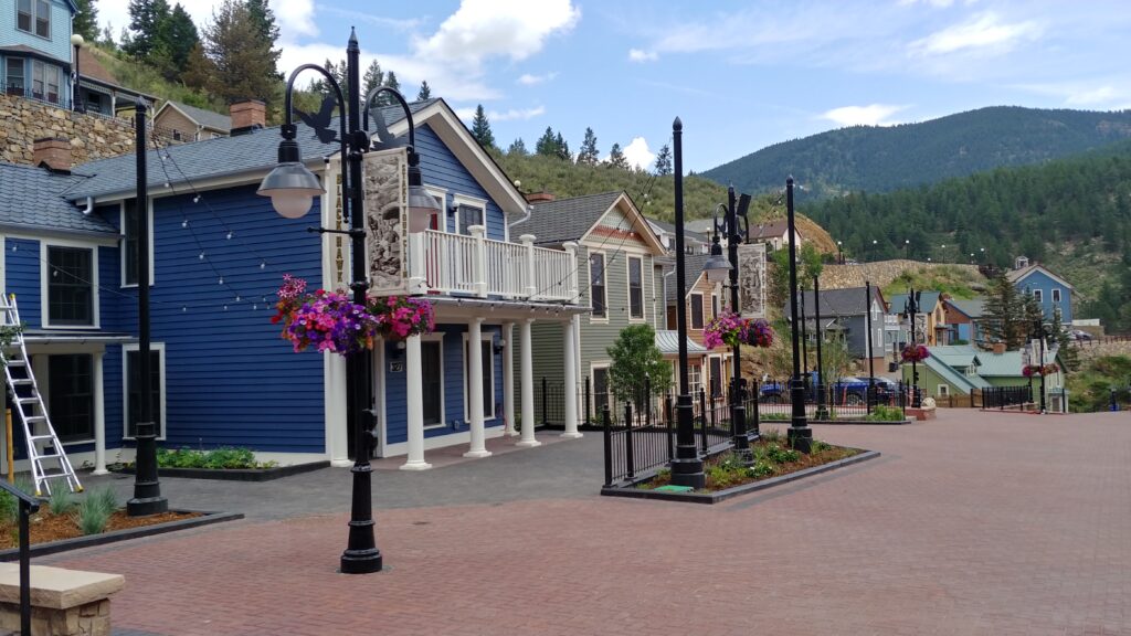 Historic town streetscape featuring colorful restored buildings, pedestrian plaza, decorative street lamps, landscaping, and mountain views