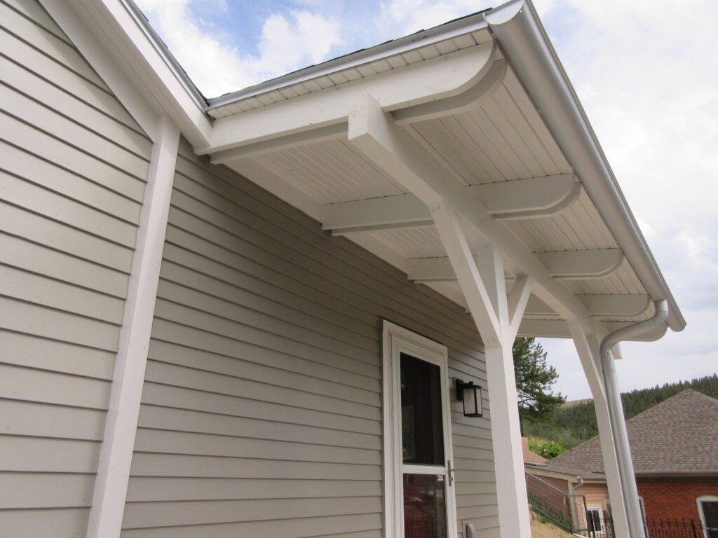 Renovated covered porch with white beams, grey siding, soffit ceiling, and modern exterior home design