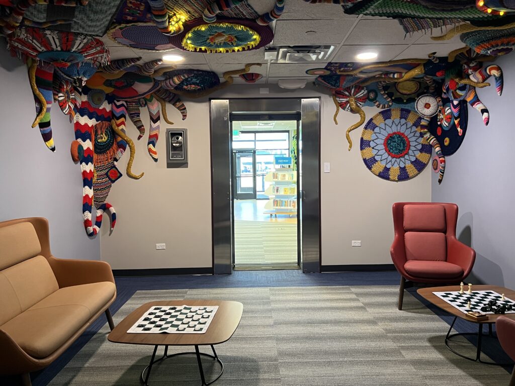 University library lounge featuring colorful textile wall and ceiling artwork, modern chairs, and chess tables