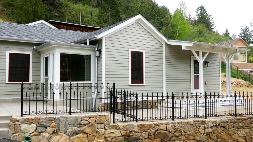Completed home exterior renovation with grey siding, covered porch, white trim, and stone landscaping