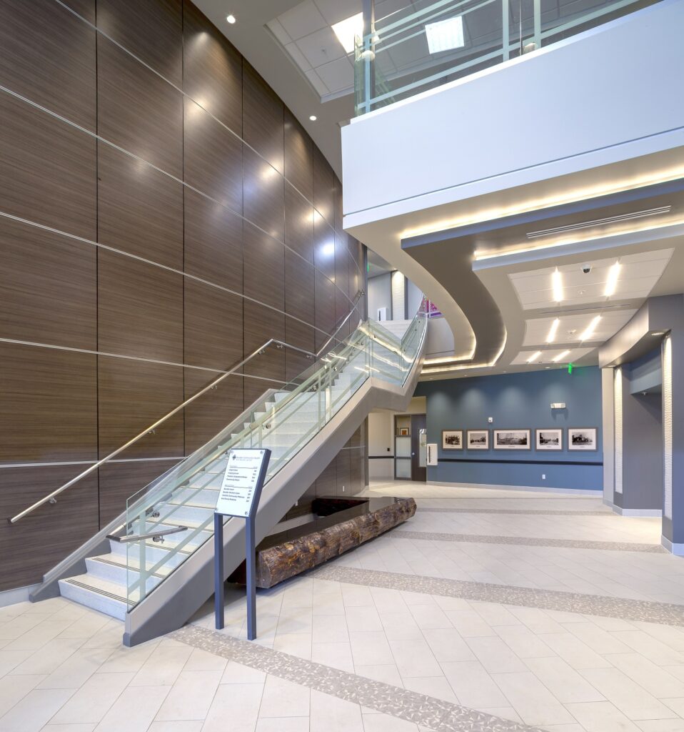 Modern healthcare facility lobby with glass staircase, architectural wall panels, open space, lighting, and contemporary interior design