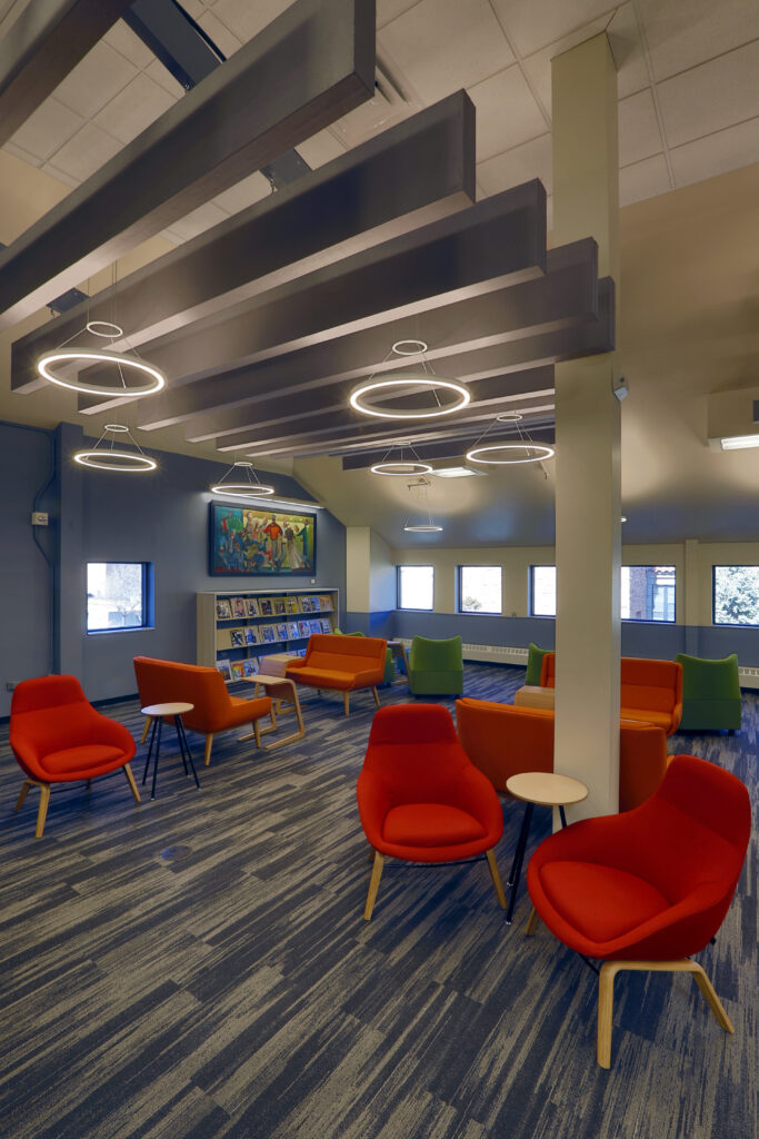 Modern university library lounge featuring colorful chairs, tables, artwork, and contemporary ceiling lighting
