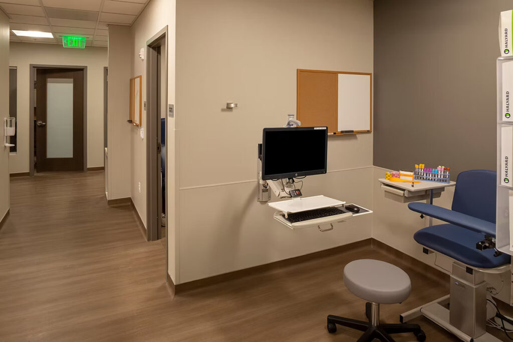 Modern medical examination room with patient chair, computer workstation, and healthcare equipment