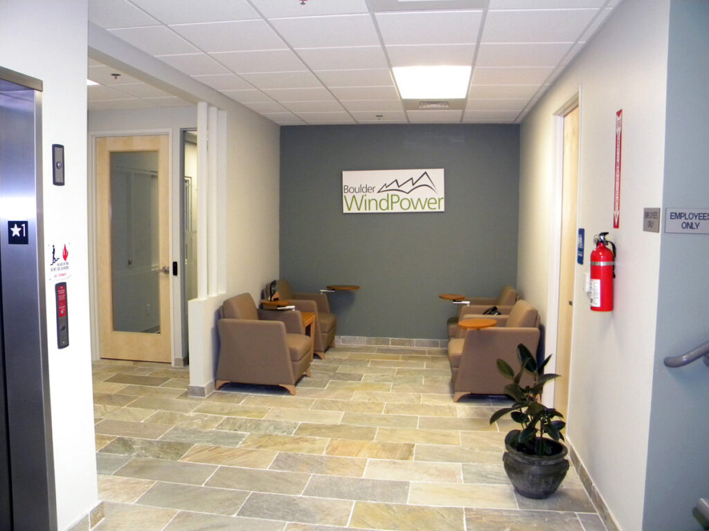 Modern office reception area with seating, tiled flooring, elevator access, and corporate branding on the wall