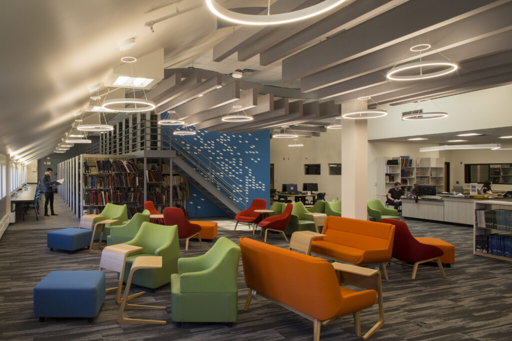 Modern university library interior featuring colorful lounge chairs, bookshelves, study desks, and contemporary lighting design