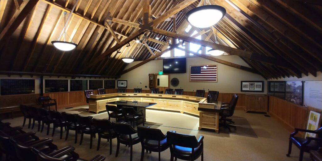 Civic meeting chamber interior featuring exposed timber beams, wood paneling, council seating, and architectural design by PEH Architects in Boulder