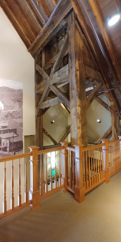 Historic building interior featuring exposed timber beams, wood railings, vaulted ceiling structure, and architectural preservation design by PEH Architects in Boulder