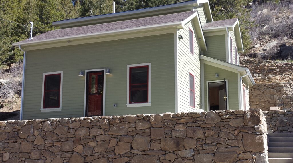 Home exterior remodeling project featuring green siding, red window trim, stone retaining wall, and modern residential design by PEH Architects in Boulder
