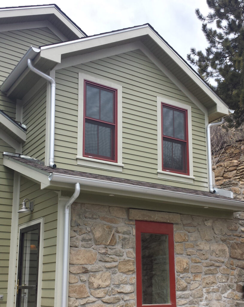 Home exterior renovation featuring green siding, stone walls, red window trim, and modern architectural details by PEH Architects in Boulder