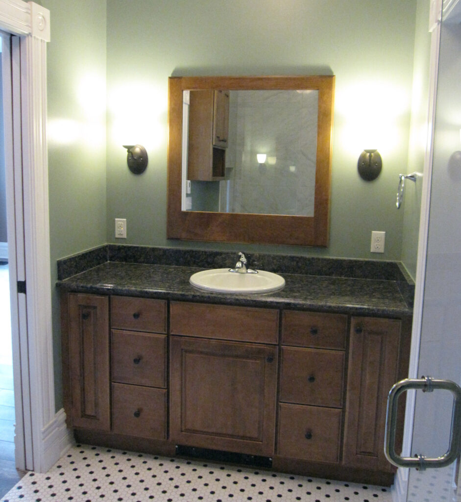 Modern bathroom renovation featuring custom wood vanity, granite countertop, framed mirror, and elegant lighting designed by PEH Architects in Boulder