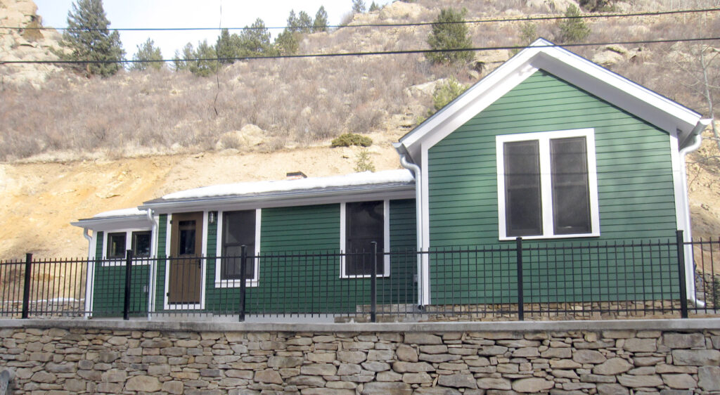 Modern home exterior renovation featuring green siding, white trim, stone retaining wall, and updated residential design by PEH Architects in Boulder