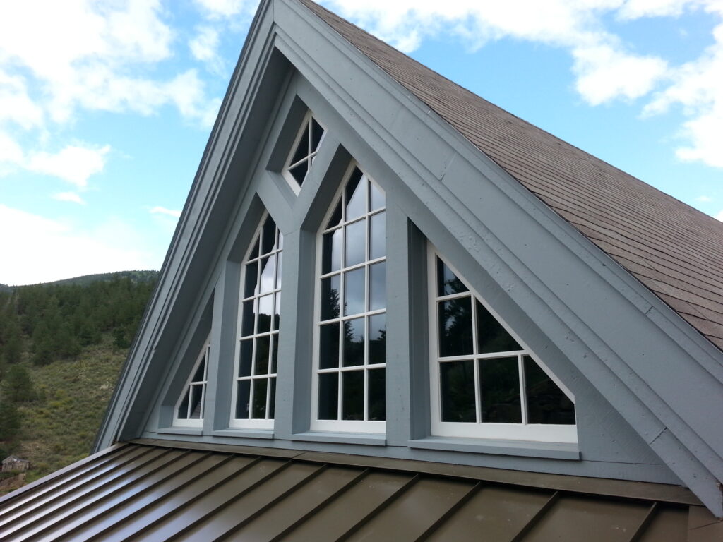 Modern home exterior featuring large gable windows, white architectural framing, metal roof details, and mountain views designed by PEH Architects in Boulder