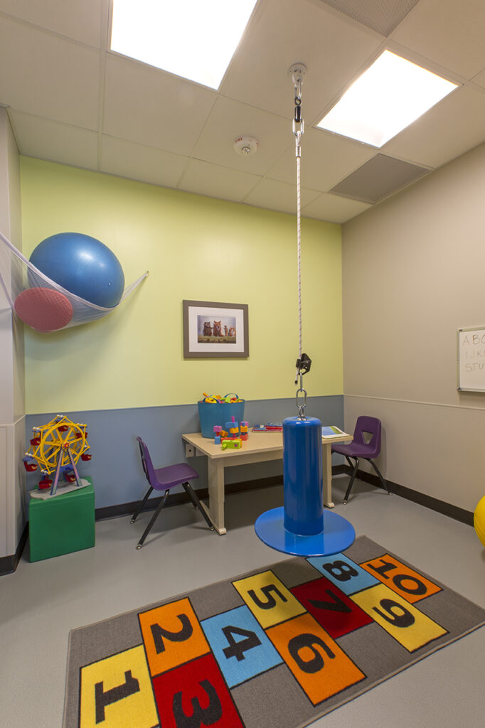 Children’s therapy room with sensory play equipment, activity table, colorful flooring, and child-friendly healthcare interior design
