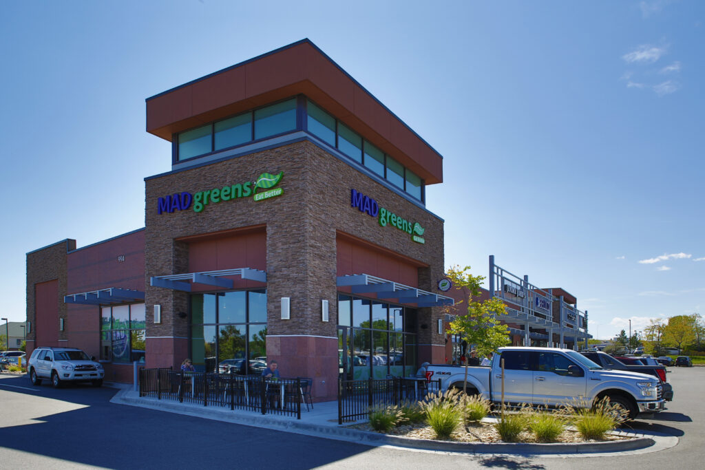 Contemporary commercial retail building exterior featuring restaurant storefronts, stone facade, glass windows, and modern architectural design