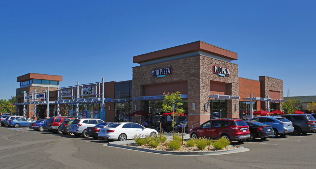 Modern commercial retail center exterior featuring contemporary storefronts, restaurants, parking area, and architectural design by PEH Architects