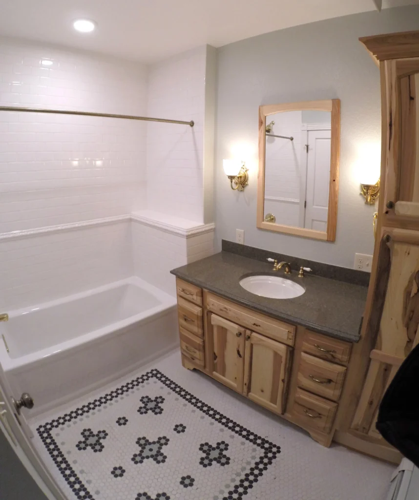 Renovated bathroom featuring custom wood vanity, granite countertop, tiled bathtub surround, decorative floor design, and modern lighting