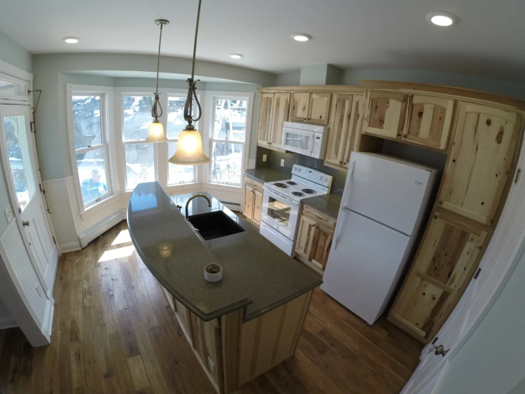 Modern renovated kitchen featuring custom wood cabinets, granite island countertop, pendant lighting, appliances, and bright interior layout