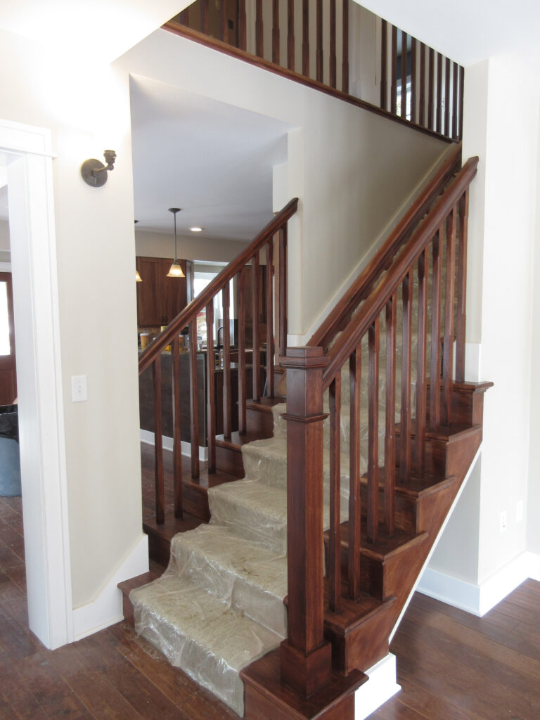 Custom residential staircase featuring wood railings, hardwood flooring, carpeted steps, and detailed interior millwork
